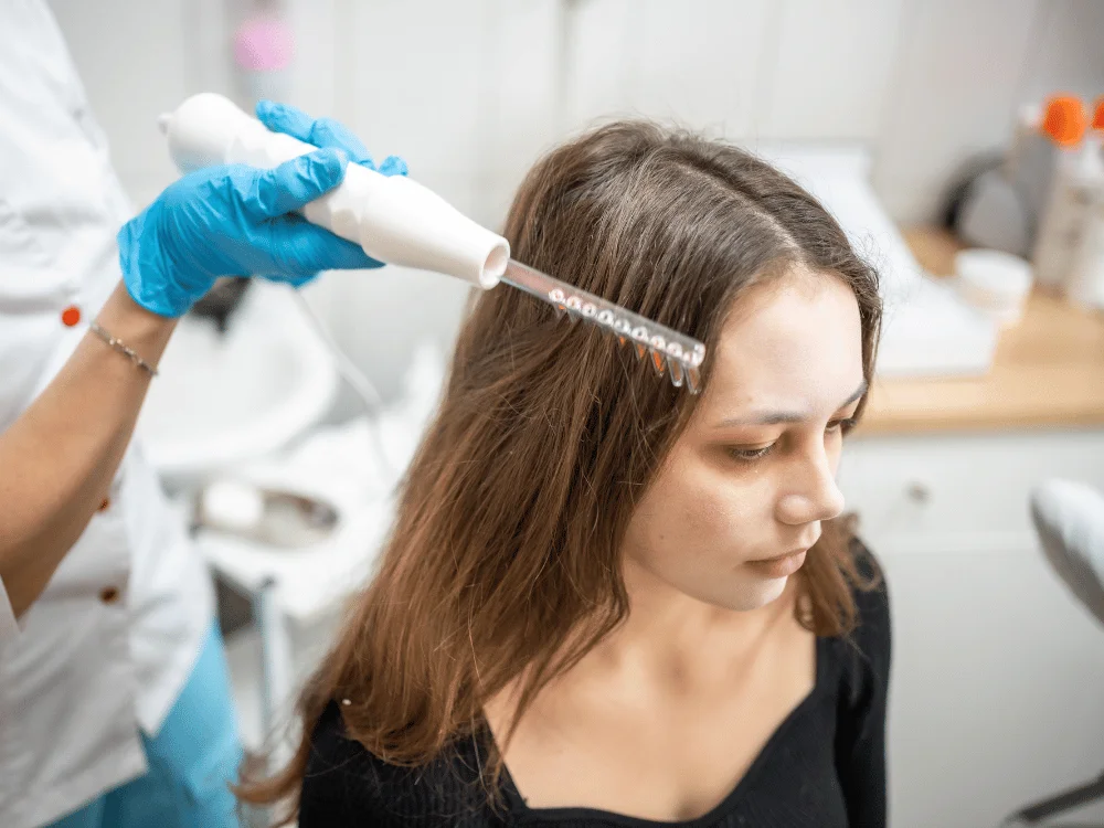 A woman receiving a scalp treatment with a handheld device as part of a non-surgical hair system procedure, aimed at promoting healthier hair growth.