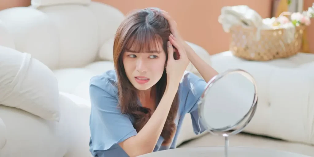 Young woman examining her scalp in mirror, visibly distressed by signs of Female Pattern Baldness.