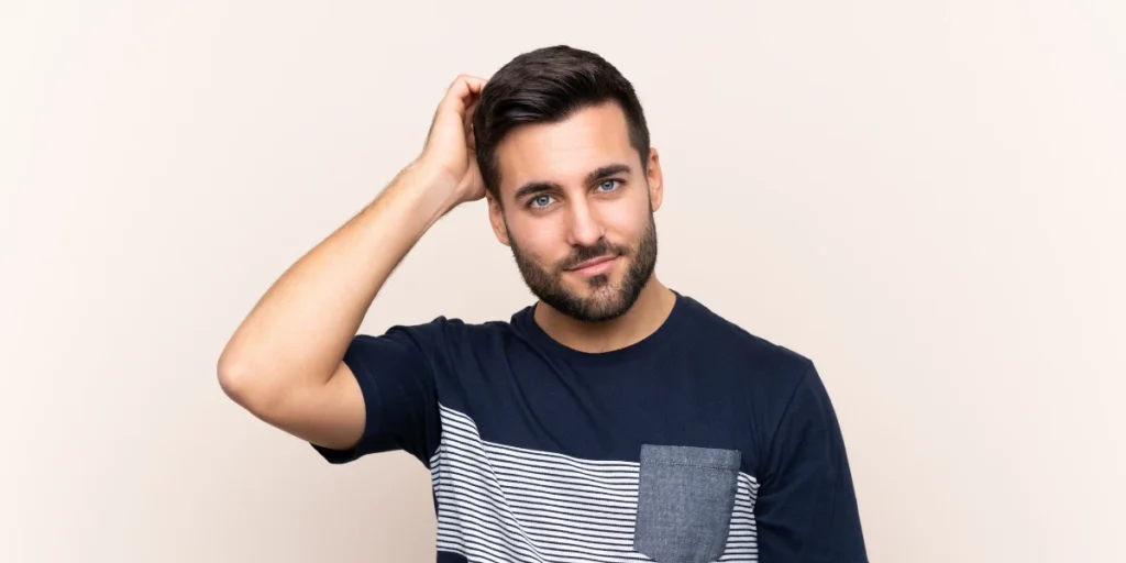 Man with styled hair and beard smiling and scratching head – Custom Hairpieces in Birmingham.