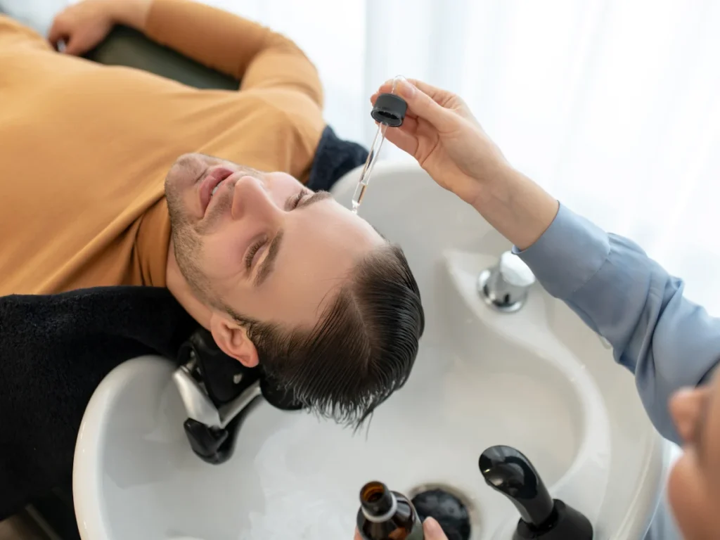 Hair System Experts in Birmingham applying serum to man's scalp at a treatment sink.