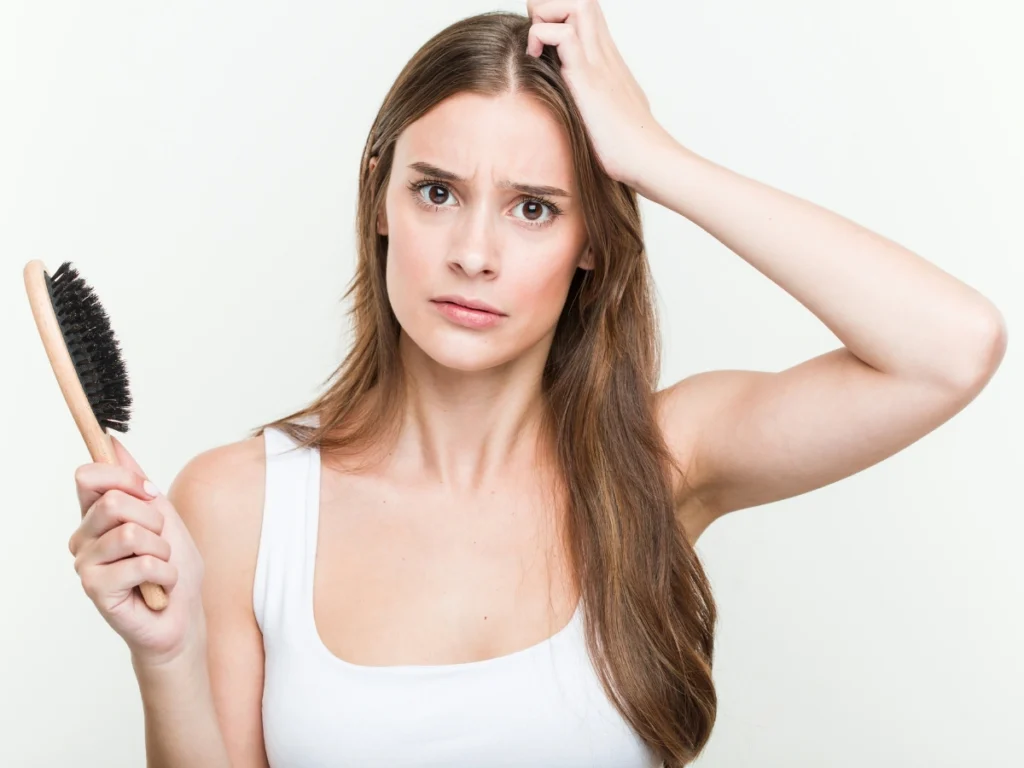 Young woman holding a hairbrush and checking her scalp, showing signs of Hair loss women UK.