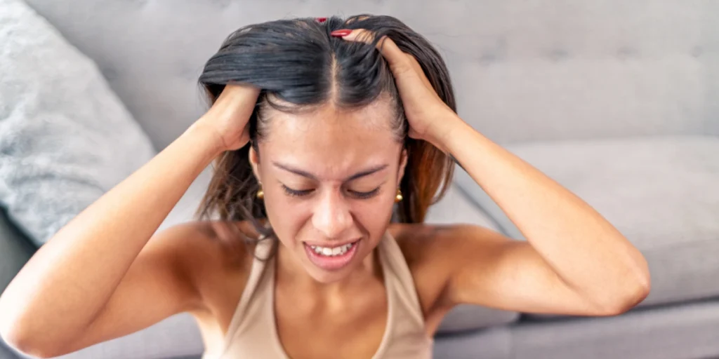 Woman holding her scalp in stress showing thinning hair and widening part, common female pattern baldness early signs