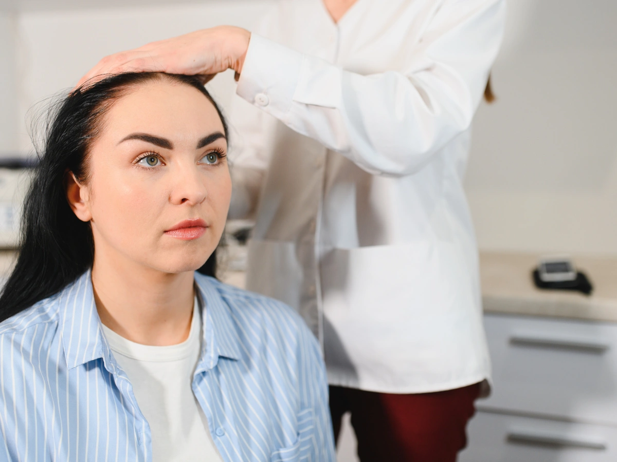 Doctor checking woman’s scalp during consultation for hair thinning and clinical signs of female pattern baldness