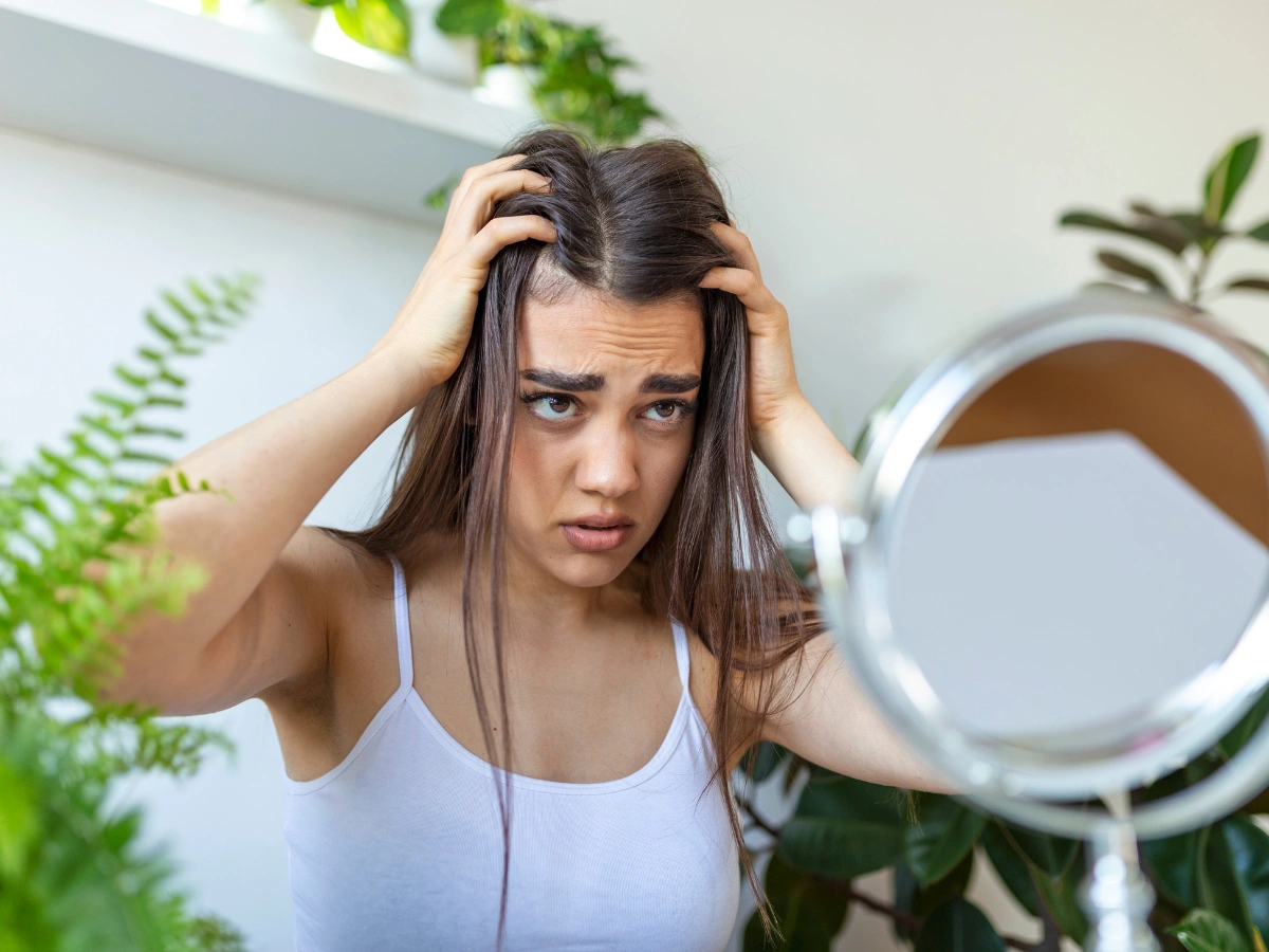 Woman distressed while examining scalp hair loss in mirror, showing signs of Trichotillomania UK.